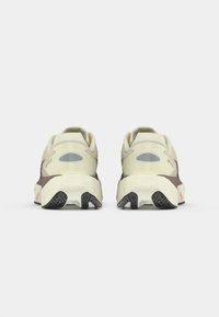 Sport shoes with a beige and brown upper, textured panels, padded heel, and a rubber outsole featuring a multi-directional tread pattern.