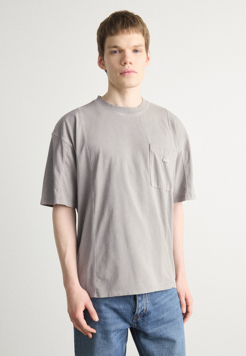 Grå bomulds t-shirt med rund halsudskæring, korte ærmer og en brystlomme. Har sidesøm og en afslappet pasform.