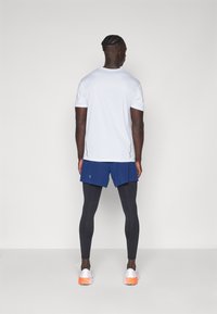 Witte kortlopende t-shirt, blauwe shorts, zwarte legging en witte sneakers met oranje accenten. Heeft een eenvoudig ontwerp en een atletische pasvorm.