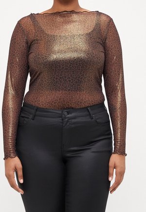 Vrouw draagt een doorschijnende, langemouwen leopardprint top met metallic glans, gecombineerd met een zwarte broek met hoge taille tegen een effen achtergrond.