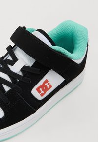 Zapatilla negra con un logo blanco y rojo, que cuenta con una correa de velcro, interior turquesa y cordones texturizados. Suela de goma con un acabado liso.