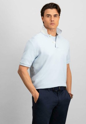 Lichtblauwe polo met korte mouwen en een knoopsluiting aan de kraag, met een contrasterende kraagband, gedragen met donkerblauwe broek.