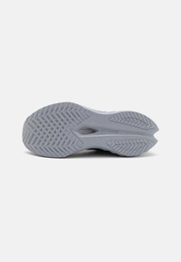 Semelle de chaussure de course gris clair avec une adhérence texturée, arborant un motif en diamant et un logo proéminent. Bords incurvés et composés en caoutchouc doubles.