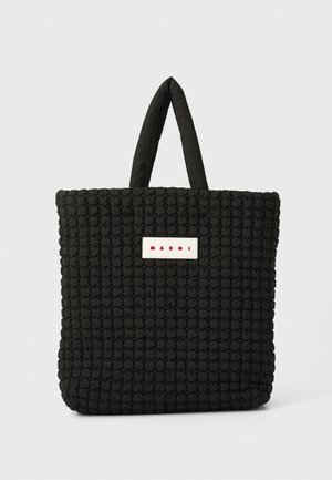 Borsa a tracolla nera trapuntata con manici imbottiti, caratterizzata da un'etichetta rettangolare bianca con lettering rosso. Superficie morbida e testurizzata.