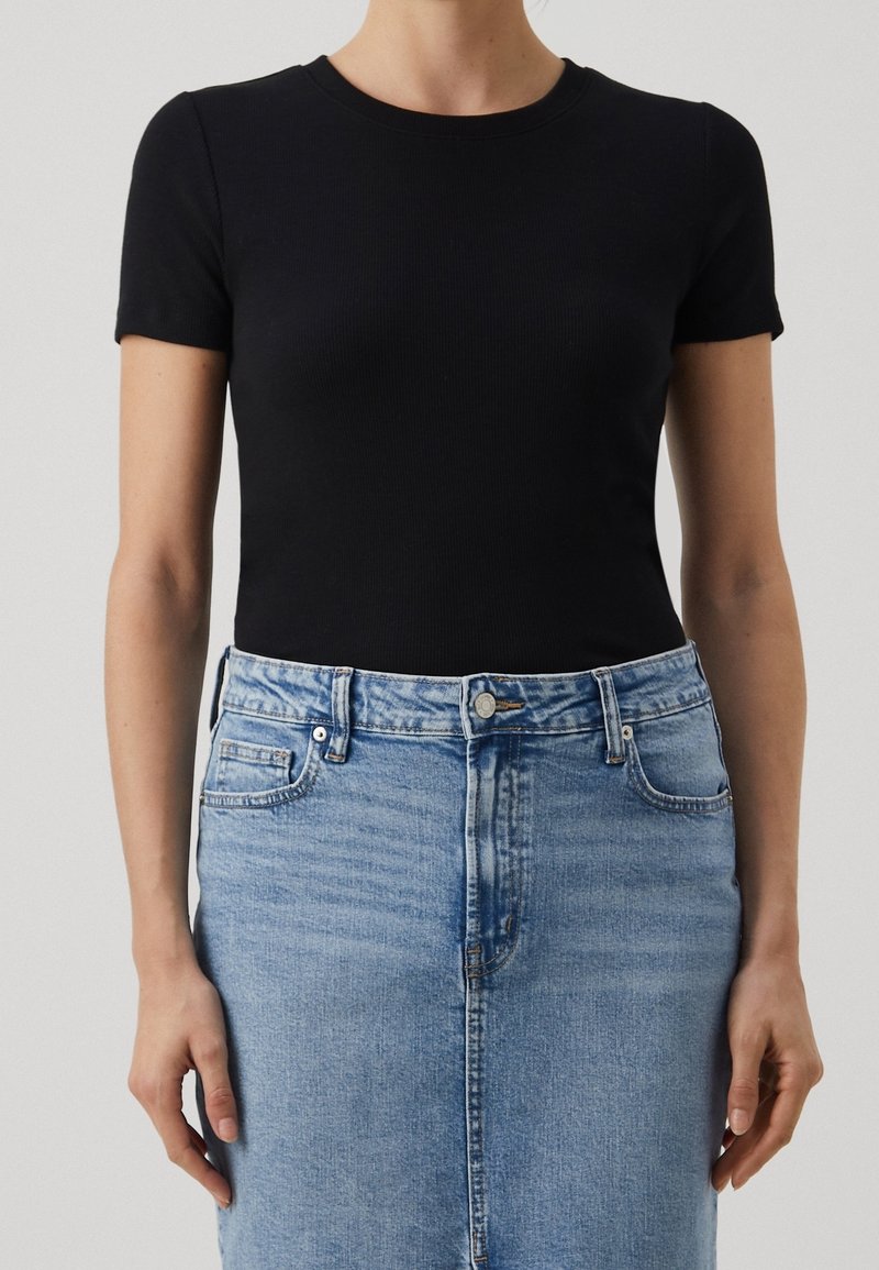 Femme portant un t-shirt noir ajusté à manches courtes rentré dans une jupe en jean bleu clair taille haute avec des poches devant.