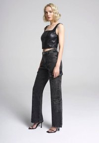 Top corto in finta pelle nera con scollatura quadrata, abbinato a pantaloni cargo grigi scuri a vita alta con tasche laterali e taglio dritto.