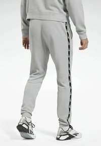 Grå ribbade sweatpants med en svart sidostrand som har ett upprepat mönster. Tyget har en mjuk textur, kompletterat av sportskor.