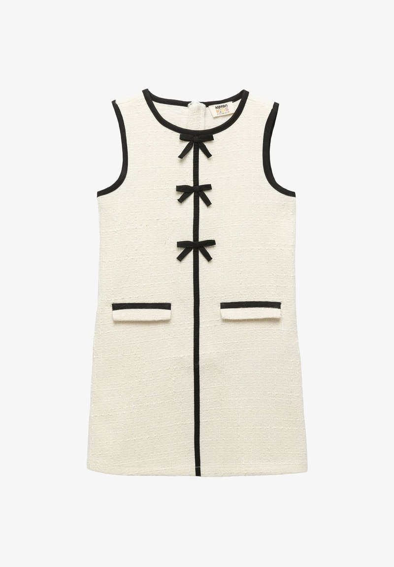 Bezramionowa sukienka w kolorze kremowym o fakturowanej powierzchni z czarnymi wykończeniami, trzy czarne kokardy na przodzie i dwie przednie kieszenie z czarnymi brzegami.