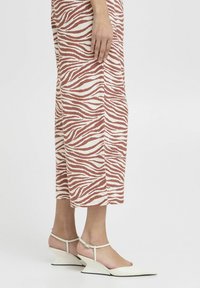 Abito midi a righe in ruggine e crema con una vestibilità rilassata; presenta una stampa zebra. Abbinato a décolleté bianche con punta affilata e tacco a zeppa.