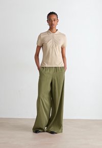 Beige polo-skjorte med en knappestolpe og korte ermer, kombinert med vide olivengrønne bukser. Antrekket har et mykt, teksturert utseende.