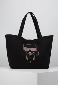 Black canvas tote bag with two handles and a central embroidered graphic of a figure wearing sunglasses, depicted in shiny thread.