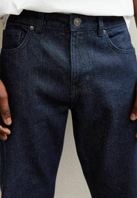 Jeans de mezclilla en azul oscuro con corte recto, que cuentan con cinco bolsillos, cierre de botón y un sutil detalle de textura.