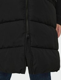 Svart pufferväst med fullängdsdragkedja, kviltat mönster och en slät, matt yta. Har isolerad vaddering och hög krage.