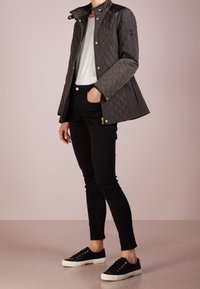 Quiltad olivgrön jacka med en figursydd passform, guldhardware och en dragkedjeförsedd fickdetalj, tillsammans med svarta skinny jeans och svarta sneakers.