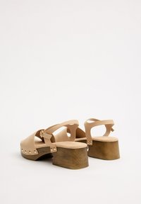 Sandalias de plataforma beige con parte superior de piel suave, correa ajustable y tacón de bloque de madera adornado con tachuelas metálicas.