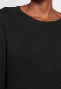 Maglione nero in maglia con scollatura rotonda, tessuto texturizzato e maniche a raglan. Nessun motivo visibile o dettagli in metallo.