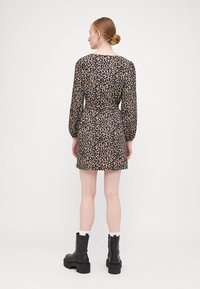 Leopardmønstret kjole med lange ærmer, en tætsiddende talje og en A-formet nederdel. Modellen har sorte kraftige støvler og hvide ankelstrømper på.