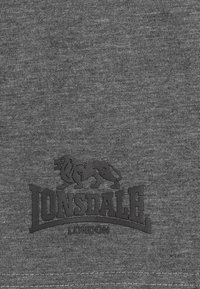 Grijze stof met een gladde textuur met een zwart Lonsdale-logo dat een leeuw afbeeldt en het woord "LONSDALE" dat gebogen boven "LONDON" staat.