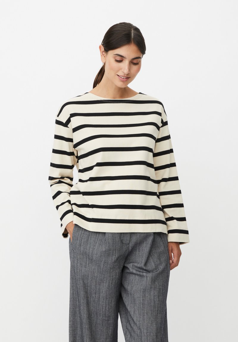 Koszula w paski z długim rękawem w kolorze kremowym z czarnymi poziomymi paskami. Miękka w dotyku, z okrągłym dekoltem i luźnym krojem. W połączeniu z szarymi plisowanymi spodniami.