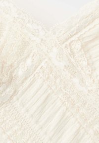 Tissu couleur crème avec des panneaux croisés de dentelle et de maille côtelée dans un motif doux et complexe.