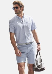 Hellblau gestreiftes kurzärmeliges Hemd mit Knopfleiste, hellblaue Shorts, gewebter Gürtel, Sonnenbrille und eine graue Tasche mit braunen Akzenten.