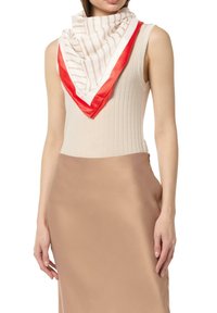 Seidenschal mit abwechselnden beigen Streifen und einem einfarbigen roten Rand. Locker um den Hals über einem hellbeigen Oberteil getragen.