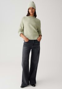 Light green, knitted sweater with a rounded neckline and ribbed hem, paired with loose, dark gray jeans and a matching beanie.