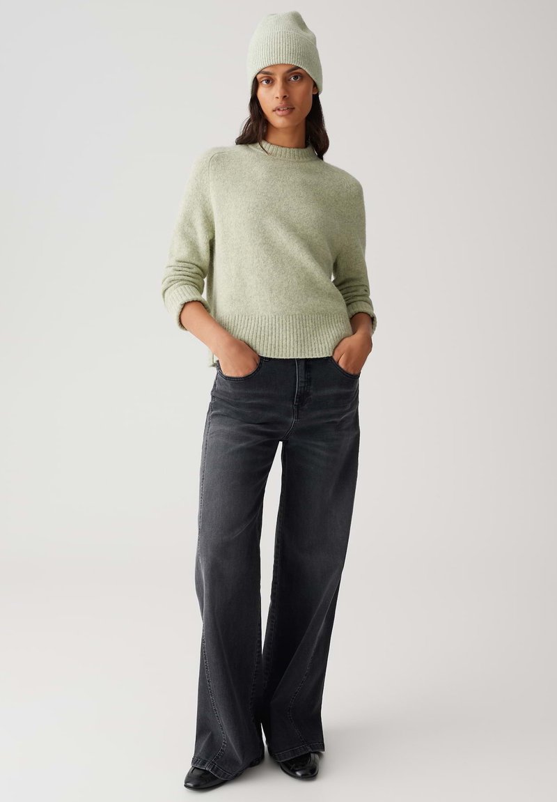 Light green, knitted sweater with a rounded neckline and ribbed hem, paired with loose, dark gray jeans and a matching beanie.