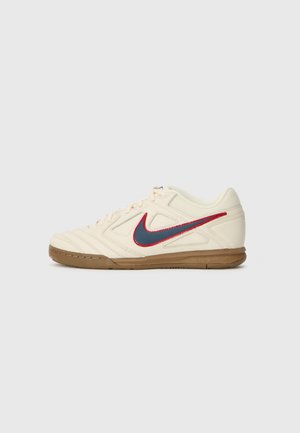Beige athletic shoes with a textured upper, red and blue swoosh accents, and gum rubber outsole; features intricate stitching and minimal design.