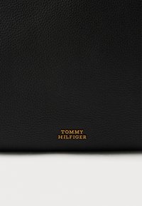 Μαύρο δερμάτινο πορτοφόλι με υφή, που φέρει το ανάγλυφο χρυσό λογότυπο «TOMMY HILFIGER». Συμπαγές ορθογώνιο σχήμα με λείο, γυαλισμένο φινίρισμα.