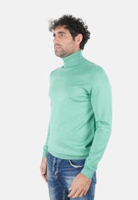 Maglione dolcevita verde menta in un materiale a maglia fine, con maniche lunghe e collo a coste. Abbinato a jeans blu distrutti.