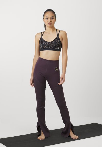 Svart sport-bh med geometriskt mönster och tunna remmar som matchas med mörk lila leggings med en logotyp och en utsvängd, delad design i nederkant.