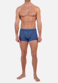 Blå bomullboxer med elastisk midjeband, med en åtsittande design och förstärkt framficka, slät textur och inga synliga mönster.