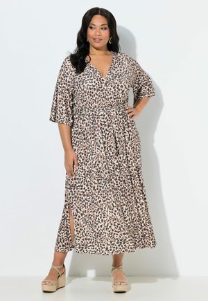 Kvinde iført en midi-kjole med leopardprint, albuelange ærmer, bindebånd i taljen, sidelomme og beige platform-sandaler, stående foran en hvid baggrund.