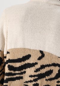 Sweter dziany z beżową górną częścią oraz dolnym wzorem zwierzęcym w odcieniach brązu i czerni, o teksturowanym wykończeniu, bez widocznych elementów metalowych.