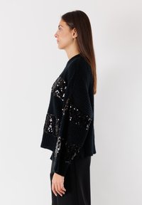 Maglione nero a maglia con vestibilità oversize, caratterizzato da strisce orizzontali in paillettes. Il tessuto testurizzato e i polsini a costine arricchiscono il design.