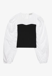 Blouse blanche à manches longues avec des manches bouffantes et des poignets élastiques, présentant un superposé ajusté en style bustier noir en côtes à l'avant.