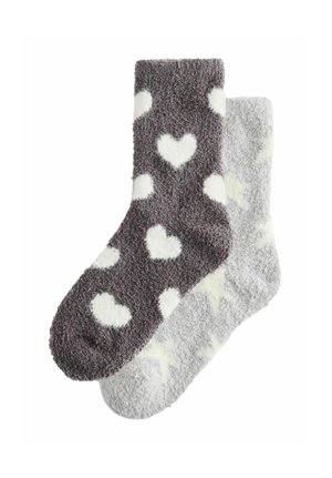 Zwei flauschige Knöchelsocken, eine dunkelgrau mit weißen Herzen, die andere hellgrau mit weißen Sternen, überlappend auf weißem Hintergrund.