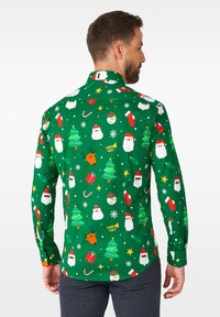 Maglietta verde a maniche lunghe con un motivo festivo di alberi di Natale, volti di Babbo Natale, renne e accenti natalizi in colori vivaci.