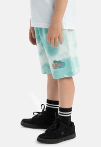 Tyrkysové šortky s technikou tie-dye a vyšívaným logom palmového stromu, spárované s čiernymi teniskami a pruhovanými ponožkami, majú jednoduchý dizajn a voľný strih.