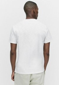 Hvid crew-neck t-shirt med korte ærmer og struktureret overflade, set bagfra. Minimalistisk design, afslappet pasform og blødt stof.