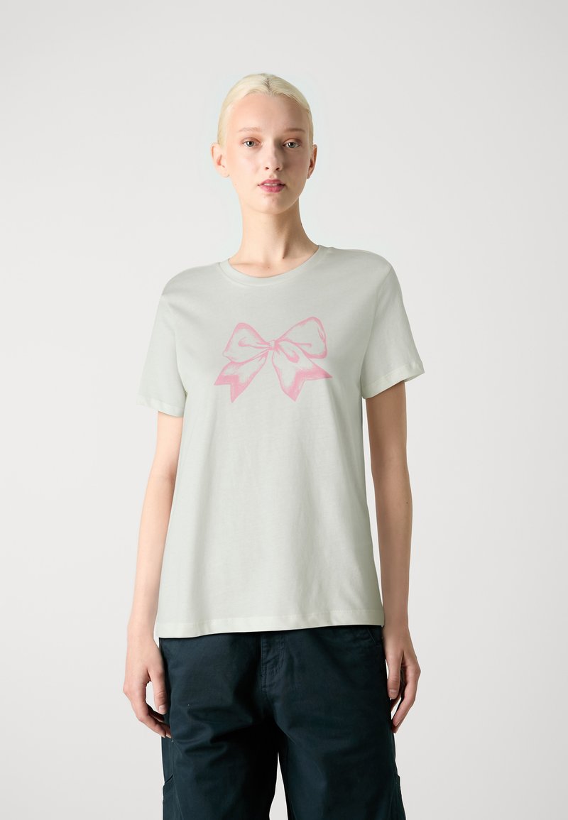 T-shirt vert clair à manches courtes en tissu doux, avec un grand graphisme de nœud rose sur le devant. Encolure ronde simple.