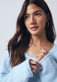 Light blue fuzzy sweater with a wide neckline and long, loose sleeves. The fabric has a soft texture and a slightly fluffy finish.