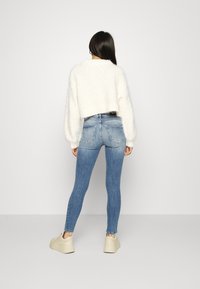 Vit, fluffig kort tröja som matchas med ljusblå skinny jeans och beige plattformssneakers. Utfälden har en avslappnad, texturerad stil.
