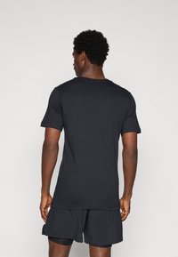 Sort bomulds T-shirt med korte ærmer, rund halsudskæring og en afslappet pasform, båret med mørke sports shorts, som viser en glat tekstur.