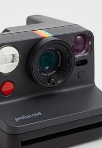Polaroid camera in black with a rainbow stripe on top; features a lens with autofocus, red button, and two flash lights.