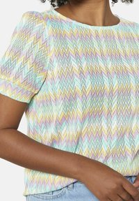 Camiseta de manga corta con un patrón en forma de chevron que presenta colores pastel de verde menta, lavanda y amarillo, confeccionada con una tela texturizada y ligera.