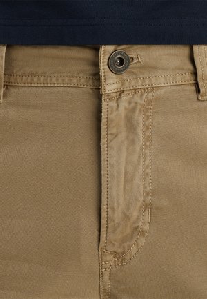 Beige bomuldsbukser med lukning foran med knap, der har en glat overflade og et enkelt design. Synlige syninger og lommer.