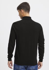 Maglione nero a maniche lunghe con colletto alto, polsini e orlo a coste. Texture liscia, design minimalista e forma aderente.