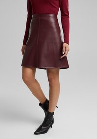 Burgundy nahka A-linja hame, jossa on sileä pinta, polven pituinen leikkaus ja minimaalinen ompelu, yhdistetty mustiin nilkkabotteihin.